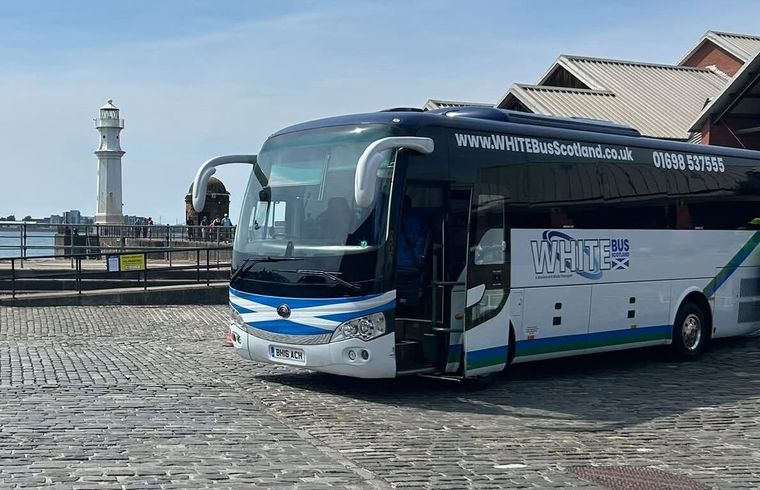 The White Bus Scotland 34-seat coach on the cobbles at Newhaven harbour, the lighthouse behind it